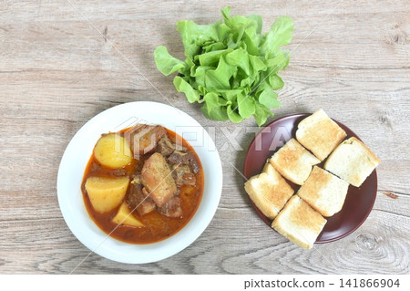 pork curry or Mussamun Indian food with slice potato on bowl eat couple fresh green oak salad and grilled butter toast bread pork curry or Mussamun Indian food with slice potato on bowl eat couple fresh green oak salad and grilled butter toast bread 141866904
