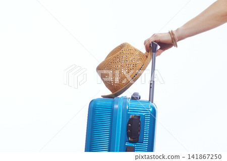 Close-up of Hand Holding Blue Suitcase with Straw Hat Close-up of Hand Holding Blue Suitcase with Straw Hat 141867250