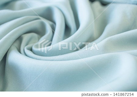 Turquoise soft silk fabric background with drapery. Pale blue fabric with twisted folds. Texture of light natural fabric, satin textile. Turquoise soft silk fabric background with drapery. Pale blue fabric with twisted folds. Texture of light natural fabric, satin textile. 141867254
