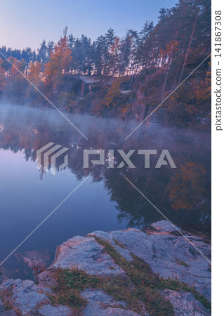 A man sitting on a wooden deck and looking at a lake with a granite shore. Sunrise over the lake A man sitting on a wooden deck and looking at a lake with a granite shore. Sunrise over the lake 141867308
