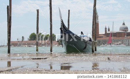 Moored gondola framed by wooden poles on Venice lagoon waterfront Moored gondola framed by wooden poles on Venice lagoon waterfront 141868112