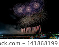 Pale blue fireworks bloom in a horizontal line across the night sky. 141868199