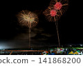 Two sets of fireworks, green and red, burst into the night sky simultaneously. 141868200