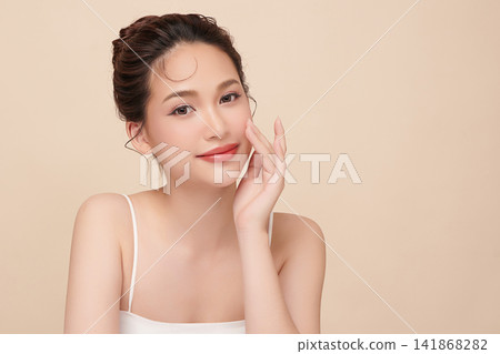 A beautiful young Asian woman with clean, fresh skin against a beige background. Skincare, facial treatment, cosmetology, beauty, and spa. An elegant portrait of an Asian woman. A beautiful young Asian woman with clean, fresh skin against a beige background. Skincare, facial treatment, cosmetology, beauty, and spa. An elegant portrait of an Asian woman. 141868282