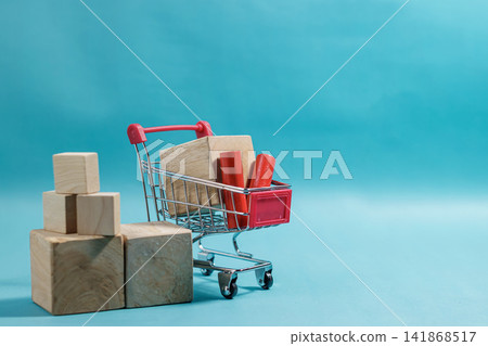 Miniature red shopping cart loaded with wooden blocks beside stacked wooden cubes on a vibrant blue background. High Quality Photo Miniature red shopping cart loaded with wooden blocks beside stacked wooden cubes on a vibrant blue background. High Quality Photo 141868517