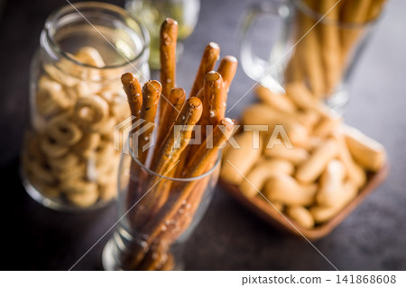 Salted Pretzel Sticks in Glass With Jars of Snacks on Dark Tabletop for Casual Snacking Salted Pretzel Sticks in Glass With Jars of Snacks on Dark Tabletop for Casual Snacking 141868608