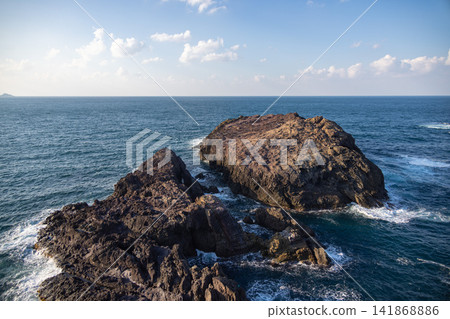 From the hilltop, one can look down upon the vast horizon and large, dark brown rock formations floating on the sea. 141868886