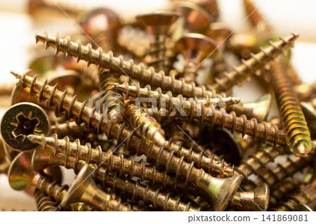 A close-up of a pile of shiny gold-colored wood screws with heads scattered randomly as a background A close-up of a pile of shiny gold-colored wood screws with heads scattered randomly as a background 141869081