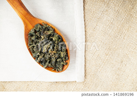 Top view closeup rustic spoon filled with loose tea on craft fabric 141869196
