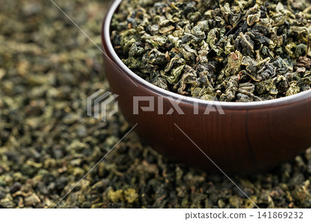 Wooden cup full of green oolong surrounded by loose tea texture Wooden cup full of green oolong surrounded by loose tea texture 141869232