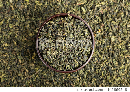Wooden cup full of green oolong surrounded by loose tea texture Wooden cup full of green oolong surrounded by loose tea texture 141869248
