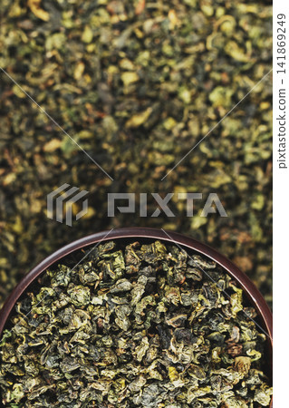 Dark wood bowl overflowing with Tie Guan Yin on full tea background Dark wood bowl overflowing with Tie Guan Yin on full tea background 141869249