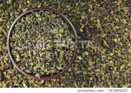 Dark wooden bowl filled with Tieguanyin on tea texture background Dark wooden bowl filled with Tieguanyin on tea texture background 141869267