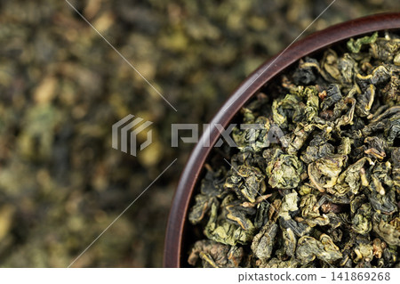 Dark wooden bowl filled with Tieguanyin on tea texture background Dark wooden bowl filled with Tieguanyin on tea texture background 141869268