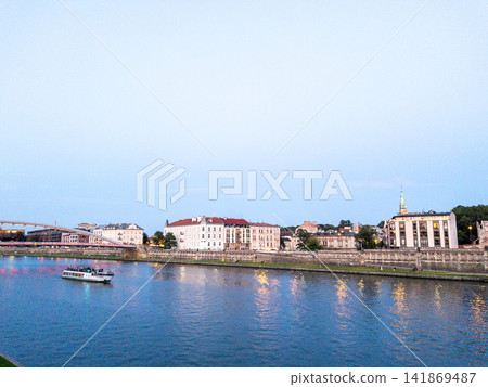 Sightseeing boat sailing on the Vistula River in Krakow, Poland at blue hour. Historic waterfront, evening cityscape, riverside promenade, travel destination, urban tourism, copy space. Sightseeing boat sailing on the Vistula River in Krakow, Poland at blue hour. Historic waterfront, evening cityscape, riverside promenade, travel destination, urban tourism, copy space. 141869487