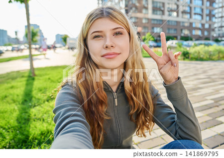 Happy young blonde woman taking a selfie and showing V peace sign Happy young blonde woman taking a selfie and showing V peace sign 141869795