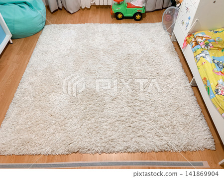 A fluffy white rug lies on a wooden floor in a child's bedroom showing soft textile textures and home decor in a bright room interior A fluffy white rug lies on a wooden floor in a child's bedroom showing soft textile textures and home decor in a bright room interior 141869904