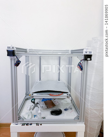 Unfinished 3D printer frame with assembled metal parts and wires standing in a bright room hobby project 141869905