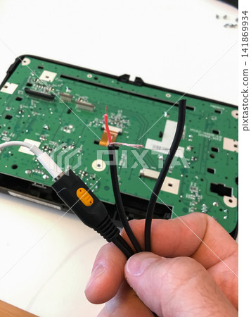 Hand holding a black connector and cables near the green circuit board of a car radio. 141869934