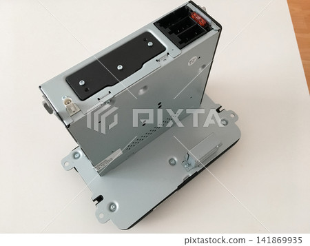 Car radio unit standing on a white table showing its metal mounting bracket and casing. Car radio unit standing on a white table showing its metal mounting bracket and casing. 141869935