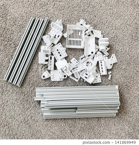 A collection of unassembled white plastic furniture components and metal support rails arranged on a carpeted floor ready for home construction project A collection of unassembled white plastic furniture components and metal support rails arranged on a carpeted floor ready for home construction project 141869949