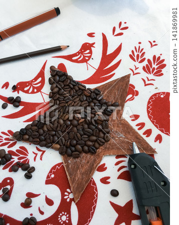 Making a coffee bean star ornament on a napkin with birds pattern and a glue gun. Making a coffee bean star ornament on a napkin with birds pattern and a glue gun. 141869981