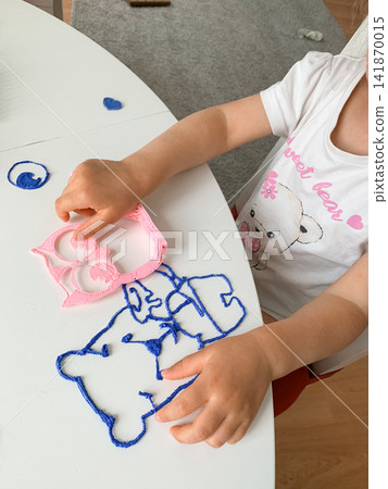 A young child sits at a white table using a 3D pen to create colorful plastic shapes of animals like an owl and a bear engaging in creative craft activities in a bright indoor home setting A young child sits at a white table using a 3D pen to create colorful plastic shapes of animals like an owl and a bear engaging in creative craft activities in a bright indoor home setting 141870015