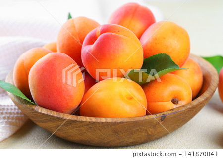 Fresh apricots in wooden bowl with green leaf on yellow textured background. Healhy food, ripe friut Fresh apricots in wooden bowl with green leaf on yellow textured background. Healhy food, ripe friut 141870041