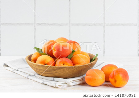 Fresh ripe apricots in wooden bowl on white kitchen table and white tiled wall with copy space Fresh ripe apricots in wooden bowl on white kitchen table and white tiled wall with copy space 141870051