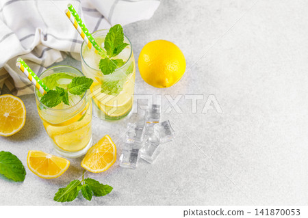 Cold homemade lemonade with fresh lemon, mint and ice in glasses on gray background, copy space Cold homemade lemonade with fresh lemon, mint and ice in glasses on gray background, copy space 141870053
