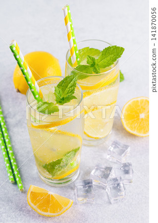 Cold homemade lemonade with fresh lemon, mint and ice in glasses on gray textured stone background Cold homemade lemonade with fresh lemon, mint and ice in glasses on gray textured stone background 141870056