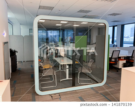 A modern glass meeting pod with chairs inside an open plan office creating a quiet space for collaboration in a corporate environment A modern glass meeting pod with chairs inside an open plan office creating a quiet space for collaboration in a corporate environment 141870139