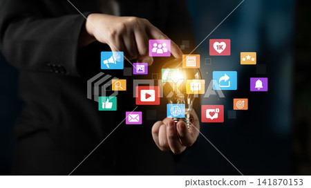 Business Professional Holding Light Bulb Surrounded by Social Media Icons Representing Innovation and Digital Communication Trends. Entropy Business Professional Holding Light Bulb Surrounded by Social Media Icons Representing Innovation and Digital Communication Trends. Entropy 141870153