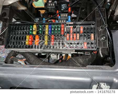 A detailed view of a car fuse box with colorful electrical fuses inserted in a black plastic holder under the dashboard A detailed view of a car fuse box with colorful electrical fuses inserted in a black plastic holder under the dashboard 141870278