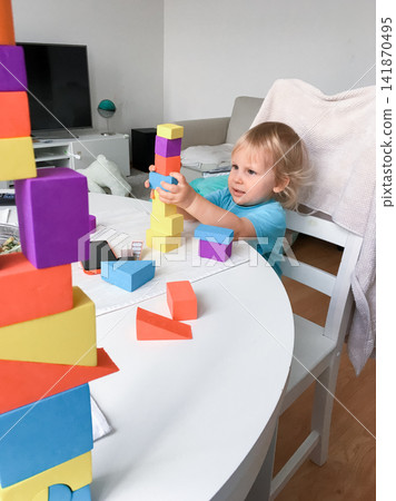 Young child playing with colorful building blocks at a table indoors. Young child playing with colorful building blocks at a table indoors. 141870495