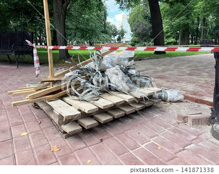 Construction waste on a wooden pallet cordoned off by red and white barrier tape in a park. City repair Construction waste on a wooden pallet cordoned off by red and white barrier tape in a park. City repair 141871338