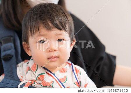 A Japanese baby boy in a watermelon-patterned jinbei participates in a festival while being carried in a baby carrier. A Japanese baby boy in a watermelon-patterned jinbei participates in a festival while being carried in a baby carrier. 141871350