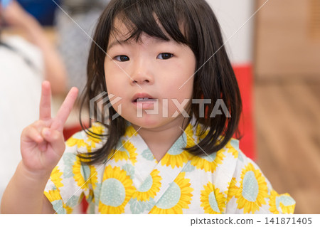 身穿向日葵圖案甚平（日本傳統夏季服裝）的日本女孩正在參加夏季祭典活動。 141871405