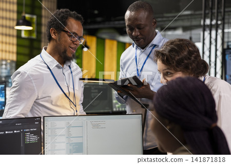 Engineering team doing brainstorming, using computer in workplace to do maintenance on neural networks. Tech startup office teamworking colleagues using AI machine learning systems on PC 141871818