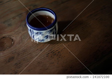 A teacup on a dark wood-grain table. Warm tea. Blue Japanese pattern. A teacup on a dark wood-grain table. Warm tea. Blue Japanese pattern. 141872100