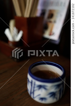 A teacup on a dark wood-grain table. Warm tea. Blue Japanese pattern. A teacup on a dark wood-grain table. Warm tea. Blue Japanese pattern. 141872102