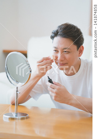 清晨,一位面帶微笑的中年男子在桌上鏡前用海綿蘸取BB霜塗抹在臉頰上——男士美容。 清晨,一位面帶微笑的中年男子在桌上鏡前用海綿蘸取BB霜塗抹在臉頰上——男士美容。 141874858