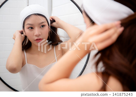 Beautiful young asian woman adjusting hair and headband with ponytail while looking mirror. Beautiful young asian woman adjusting hair and headband with ponytail while looking mirror. 141875243