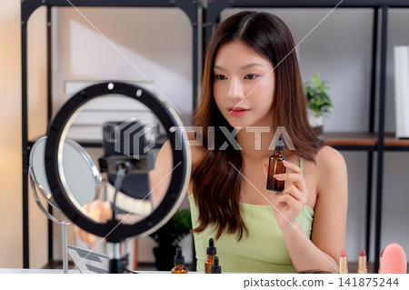 Young asian woman demonstrating serum on hands on social media at home. Young asian woman demonstrating serum on hands on social media at home. 141875244