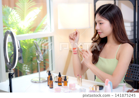 Young asian beauty influencer testing multiple lipstick shades on arm while recording makeup review. 141875245