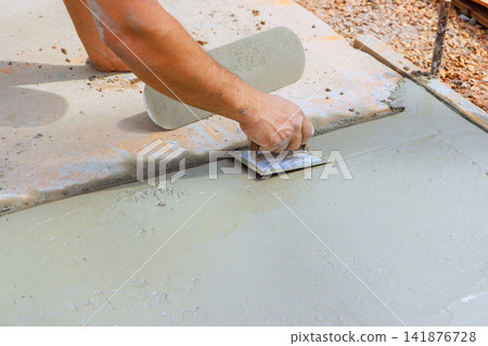 Contractor is smoothing fresh wet concrete with trowel on worksite Contractor is smoothing fresh wet concrete with trowel on worksite 141876728
