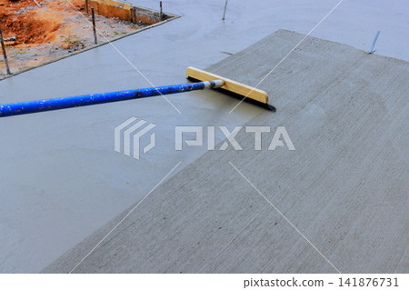 Worker is leveling wet concrete using trowel broom at construction site Worker is leveling wet concrete using trowel broom at construction site 141876731