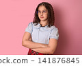 Confident Young Girl in Casual Outfit Posed Against a Bright Pink Background with Arms Crossed 141876845