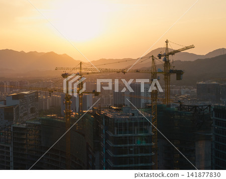 Large yellow construction cranes towering over urban residential buildings during a golden sunset near mountains in the city of China Large yellow construction cranes towering over urban residential buildings during a golden sunset near mountains in the city of China 141877830