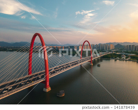 Cars drive across the large red steel arched bridge over the calm Qiantang River in Hangzhou during a bright sunset 141878439